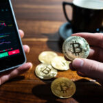 Wykresy na telefonie oraz moneta z symbolem Bitcoina