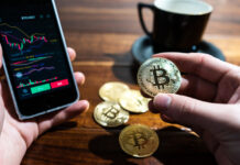 Wykresy na telefonie oraz moneta z symbolem Bitcoina